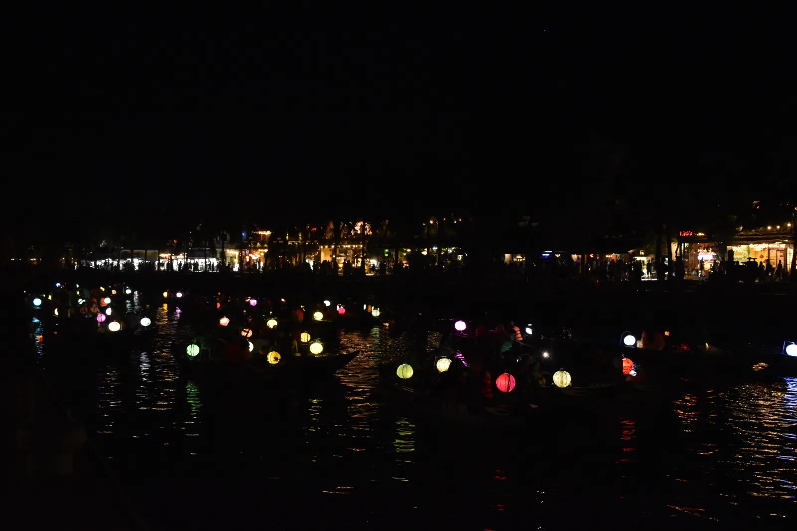 Lantern-lit boats moving along the river in Hoi An at night
